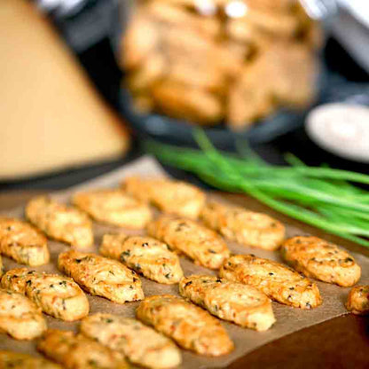 Kekse auf Backpapier mit Schnittlauch im Hintergrund.