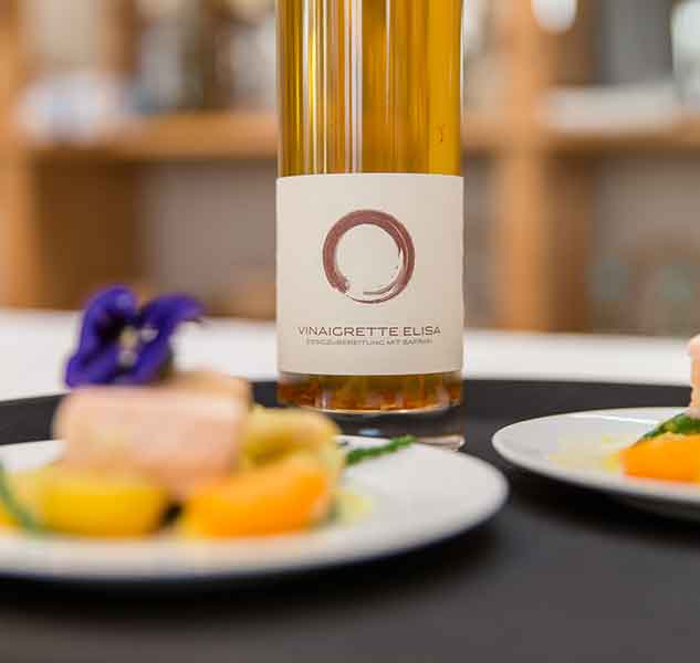 Flasche Vinaigrette Elisa mit Speisen im Hintergrund.