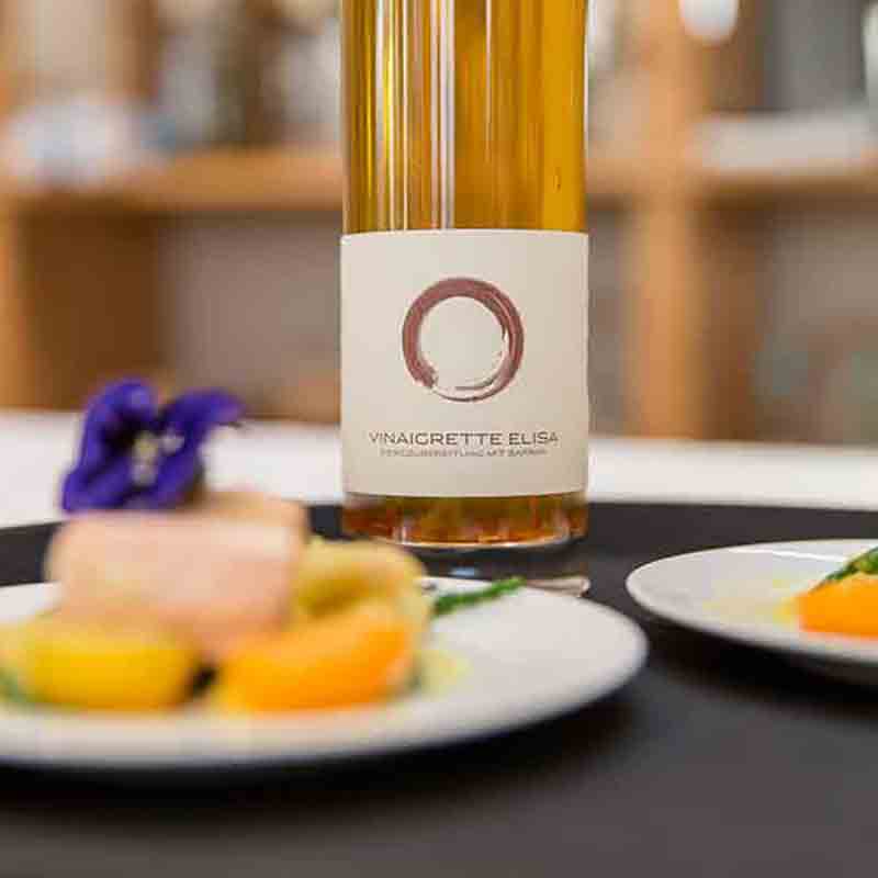 Flasche Vinaigrette Elisa, Teller mit Feinkost im Vordergrund.