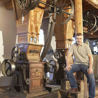 Mann neben traditioneller Ölpresse sitzend.