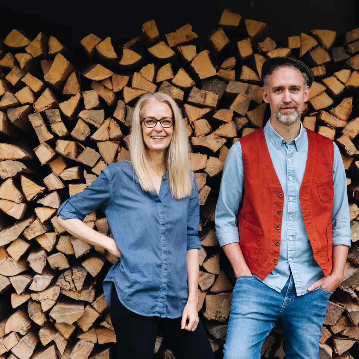 Zwei Personen vor Holzstapeln.