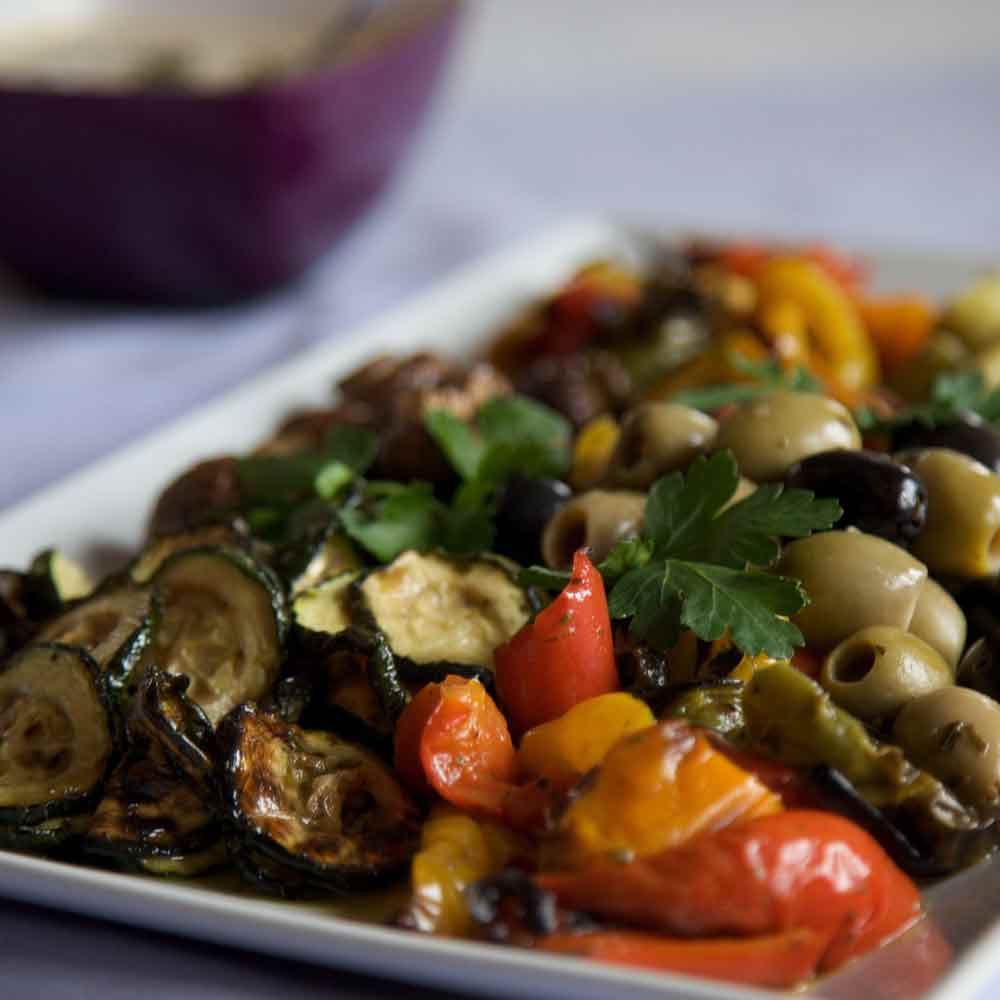 Antipastiteller mit Oliven, Zucchini, Paprika und Petersilie.