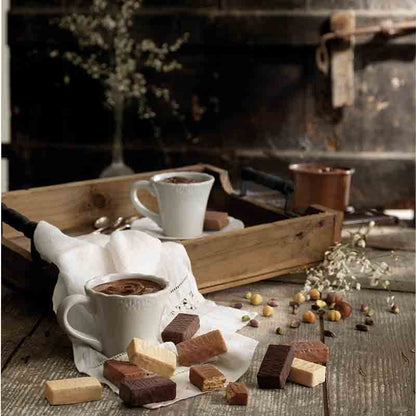 Feinkostpräsentation mit Tassen, Schokolade und Nüssen auf Holztisch.