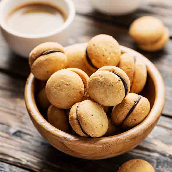 Holzschale mit Baci di Dama Keksen auf Tisch.