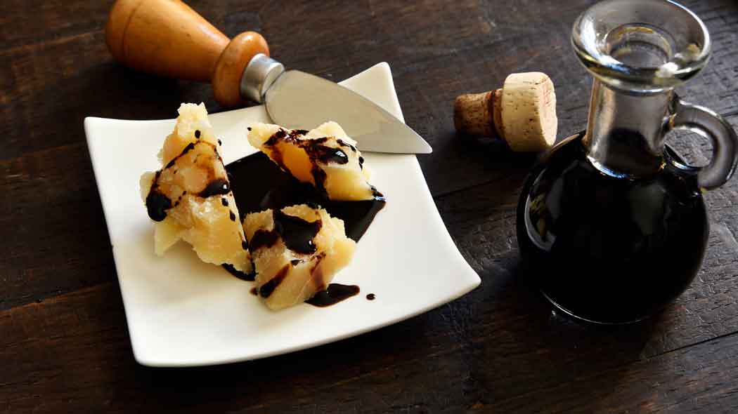 Parmesan mit Balsamico und Messer auf Holztisch.