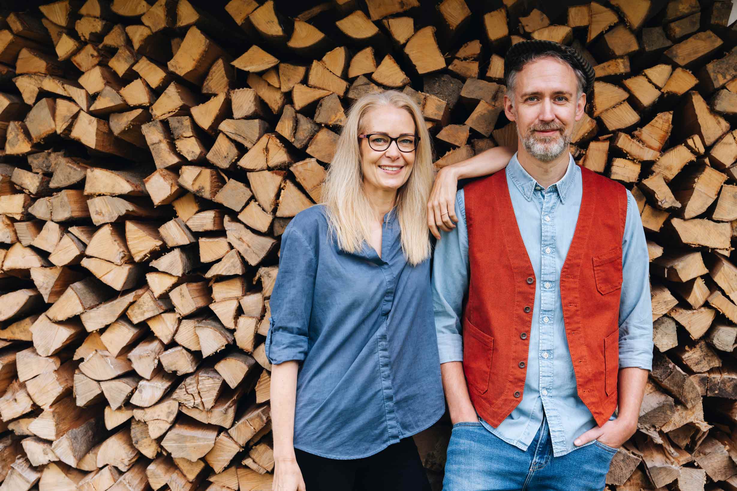 Zwei Personen vor Holzstapel.