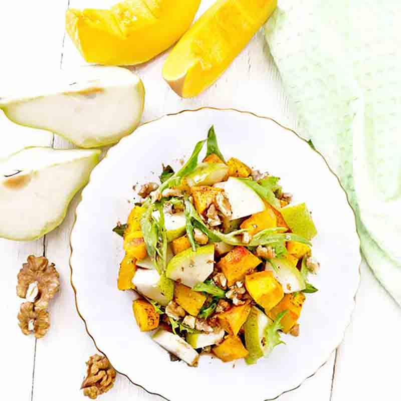 Salat mit Birnen, Walnüssen und Kürbis auf weißem Teller.