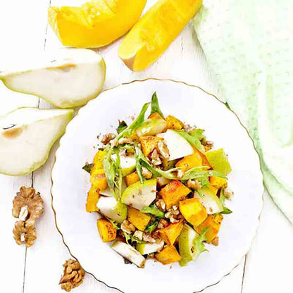Salat mit Birnen, Walnüssen und Kürbis auf weißem Teller.