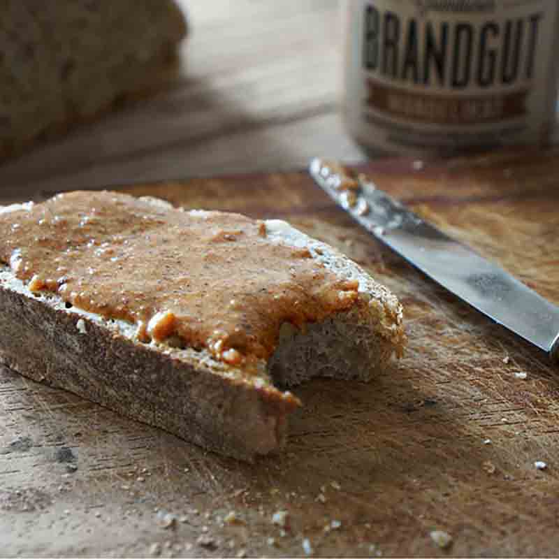 Brot mit Aufstrich, Messer, Brandgut-Glas im Hintergrund.