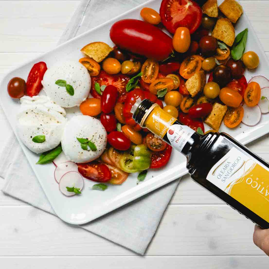 Teller mit Tomaten, Mozzarella, Brot, Olivenöl-Flasche.