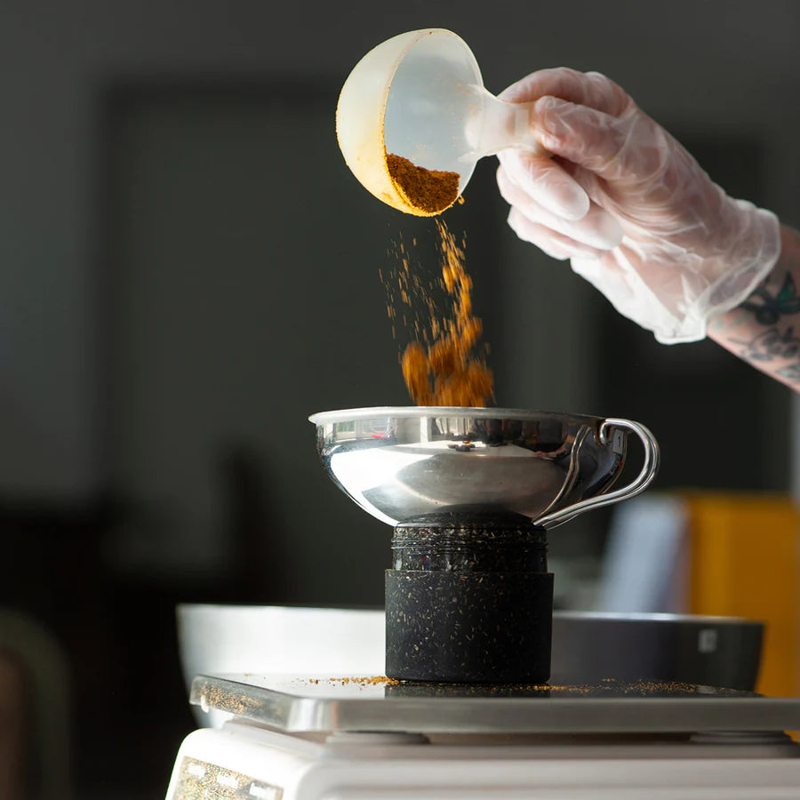 Hand füllt Gewürze in Behälter mit Trichter.