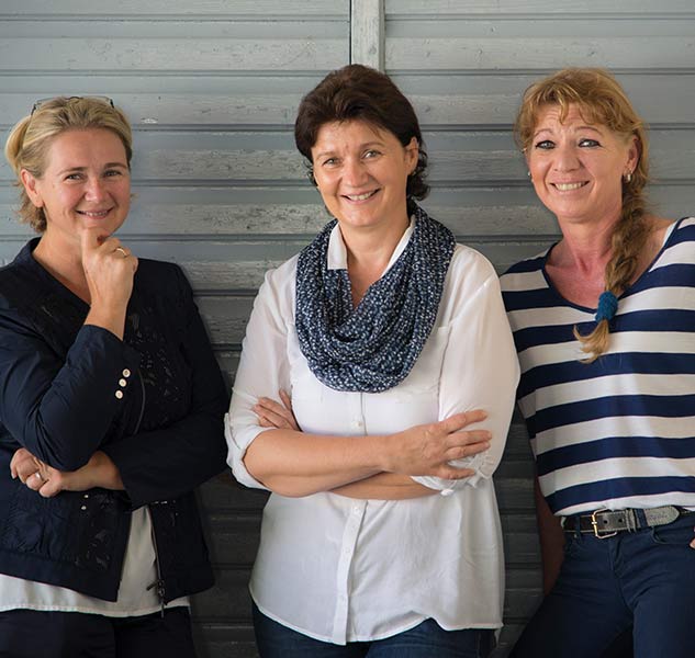 Drei lächelnde Frauen vor Wand.