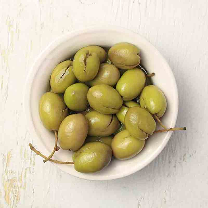 Schale mit entkernten grünen Oliven auf hellem Hintergrund.