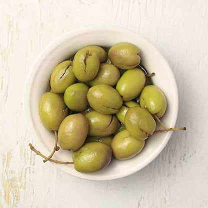 Schale mit entkernten grünen Oliven auf hellem Hintergrund.