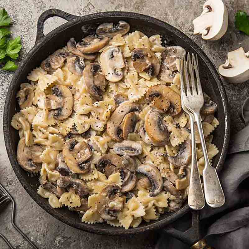 Farfalle mit Pilzen in Pfanne.