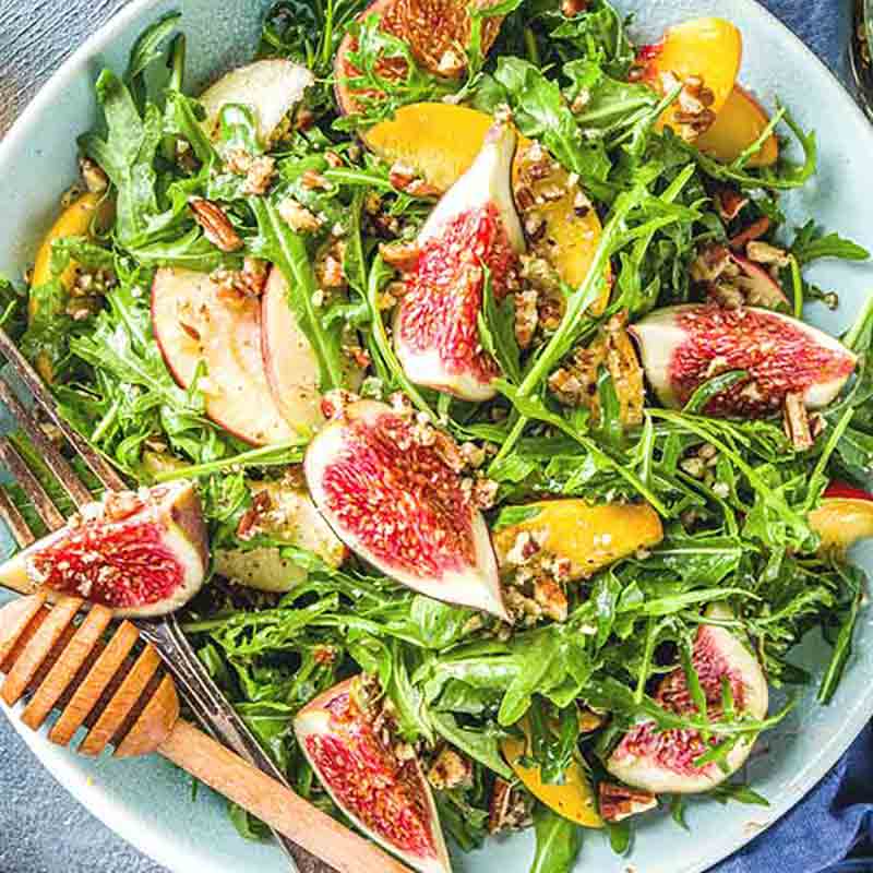 Feigensalat mit Rucola, Nüssen und Essig auf Teller.