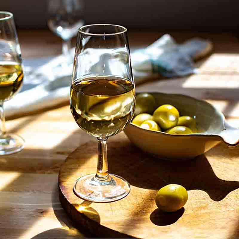 Weinglas und Schale mit gefüllten Oliven auf Tisch.