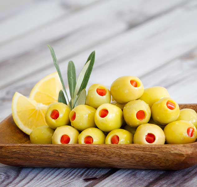 Gefüllte grüne Oliven mit Paprika auf Holzplatte.