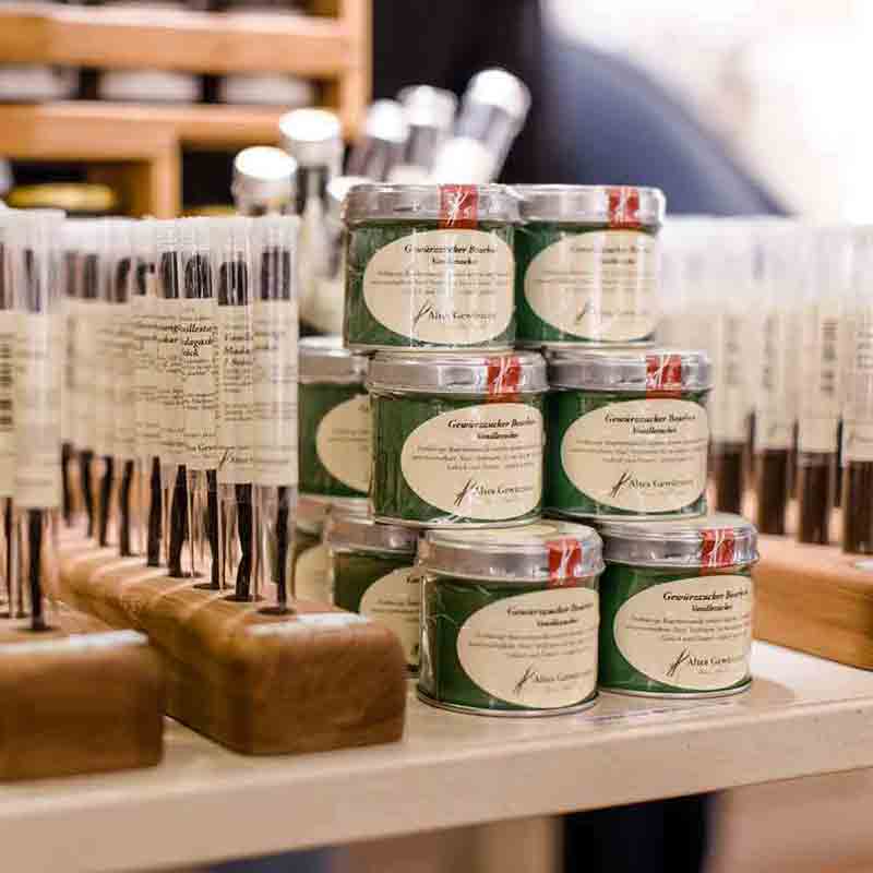 Feinkostladen mit Gewürzdosen und Essigflaschen auf Holztisch.