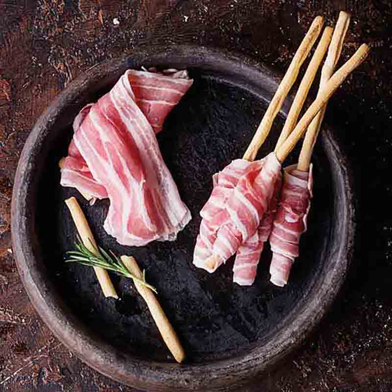 Grissini mit Schinken auf dunklem Teller, Rosmarin-Zweig.