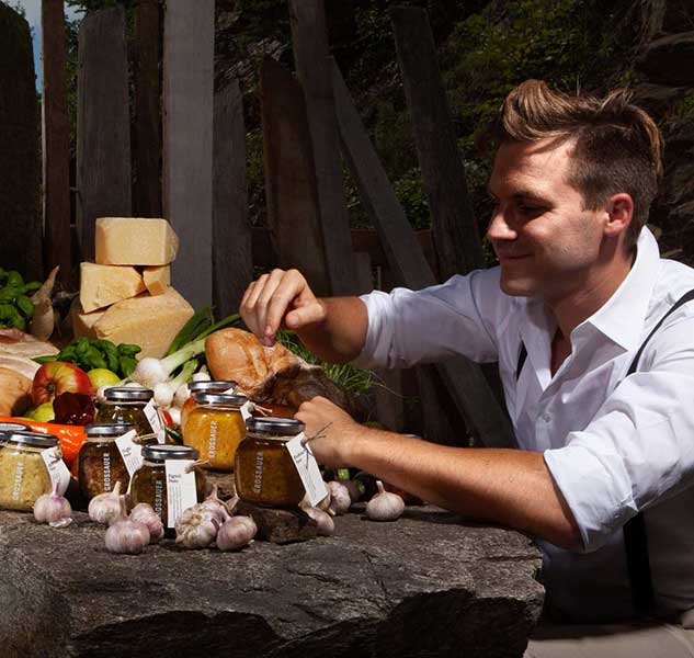 Feinkostprodukte auf Steintisch mit Mann im Hintergrund.