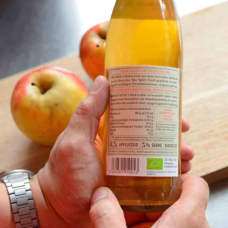 Person hält Apfelessigflasche vor Äpfeln.