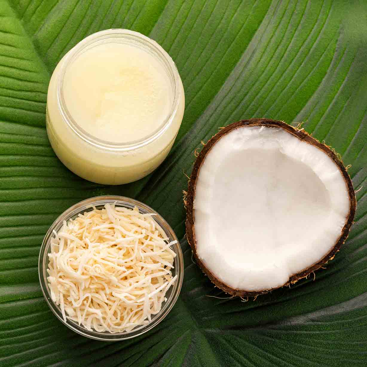 Kokosöl, Kokosnuss und geraspelte Kokosnuss auf Blatt.
