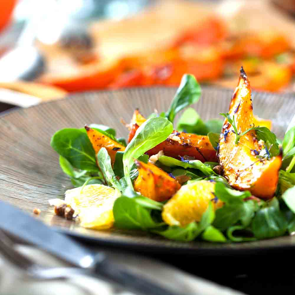 Salat mit Kürbis, Orangen und Blattsalat auf Teller.