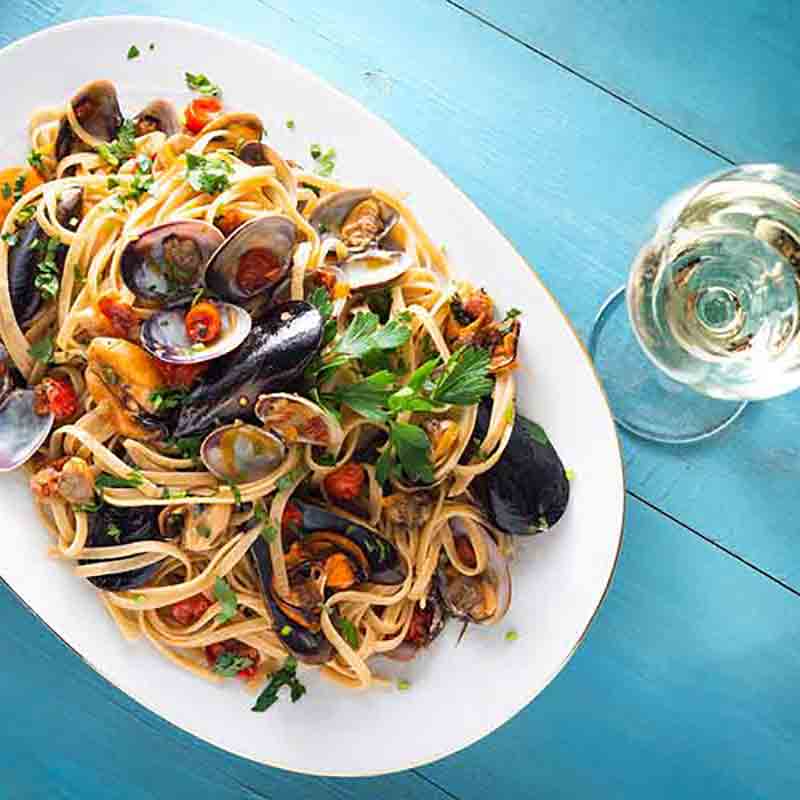 Linguine mit Meeresfrüchten und Glas Weißwein auf Tisch.