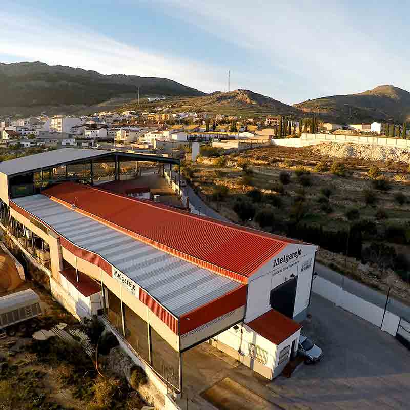Blick auf die spanische Ölmühle vom Melgarejo mit rotem Dach. Im Hintergrund sieht man sanfte Hügel.