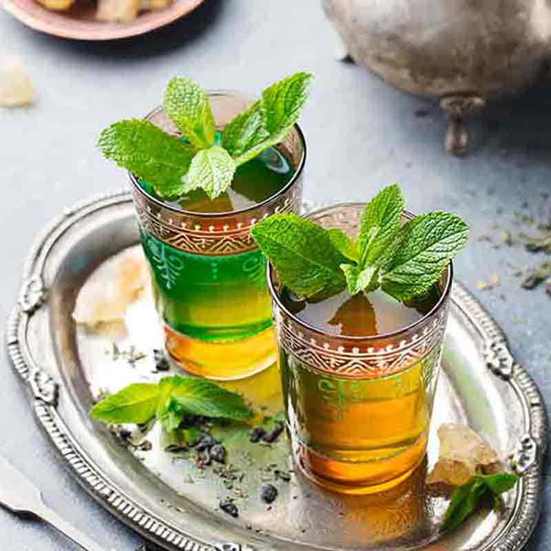 Zwei Gläser Tee mit Minze auf einem Tablett.