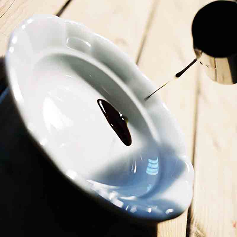 Essig wird in weißen Teller gegossen, Holzuntergrund sichtbar.