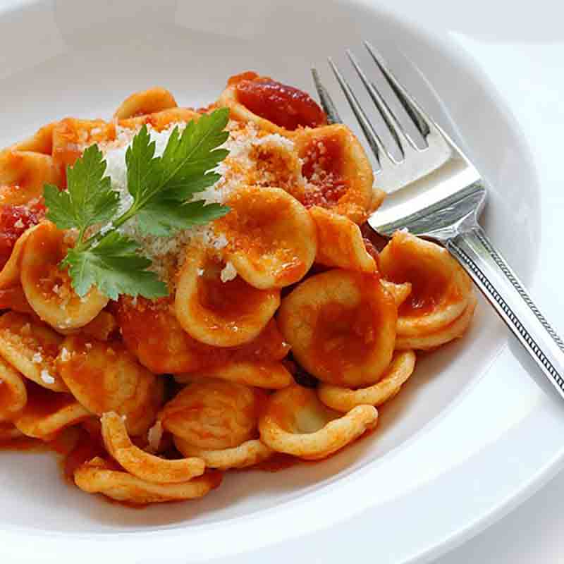 Orecchiette mit Tomatensauce und Petersilie auf weißem Teller.