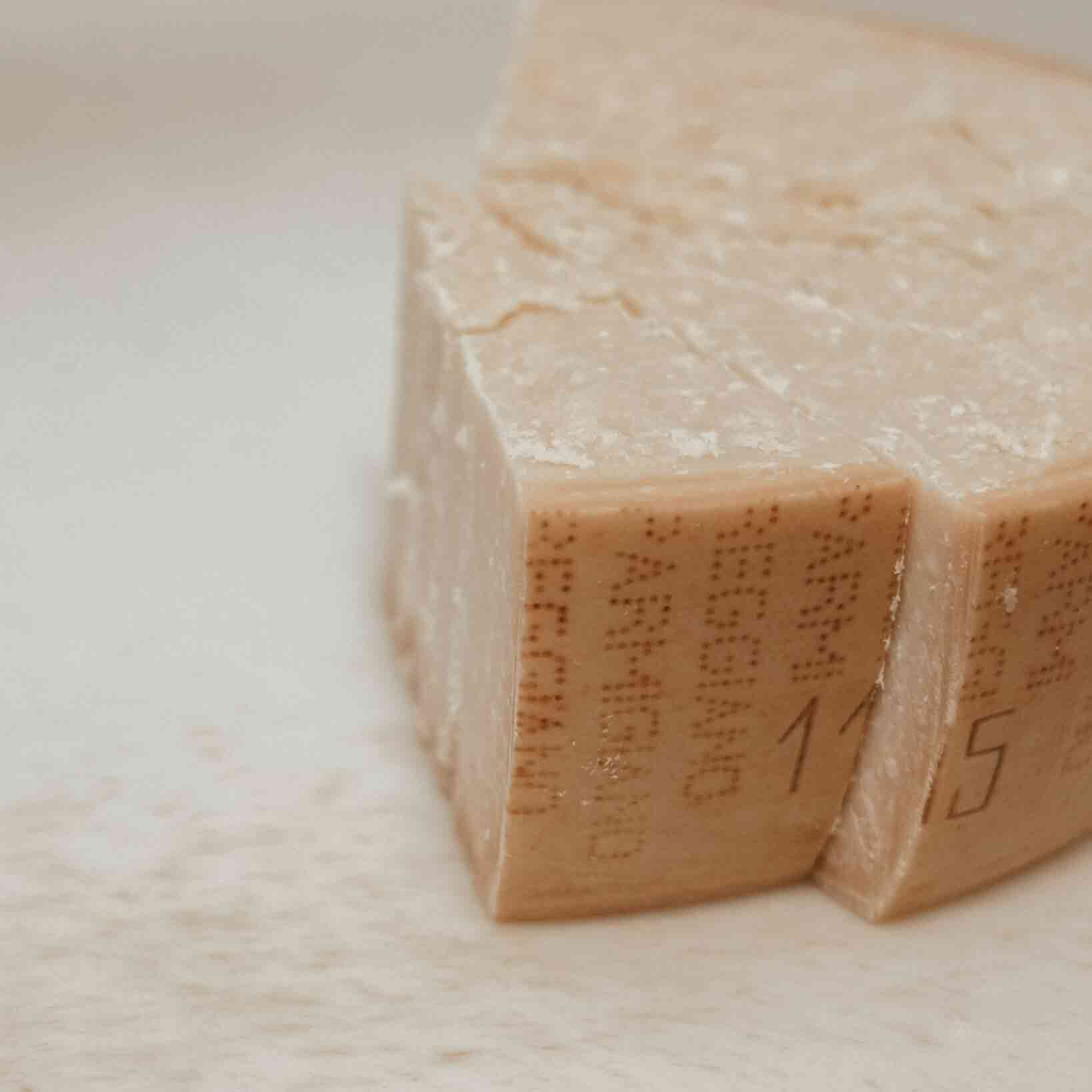 Käseblock mit Aufschrift "Parmigiano Reggiano" auf hellem Hintergrund.