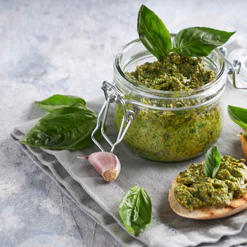 Pesto im Glas mit Basilikum und Knoblauch auf Tuch.