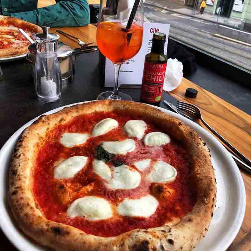 Pizza mit Chiliöl-Flasche und Getränk auf Tisch.