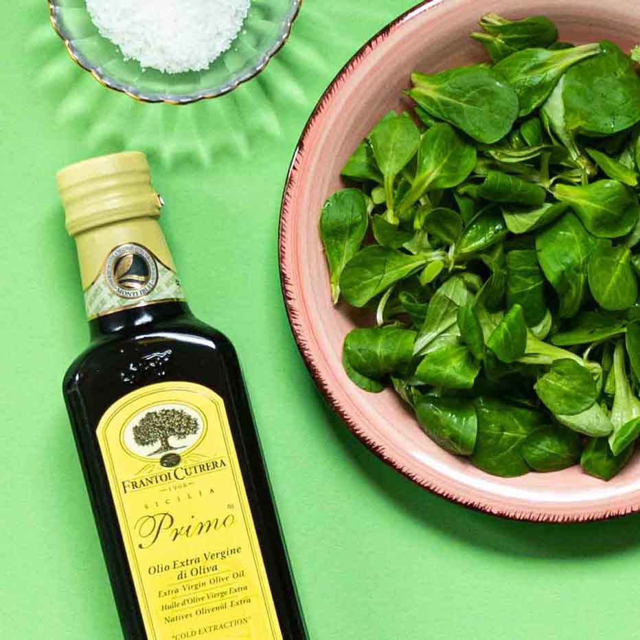 Olivenöl, Feldsalat, Salz in Schale auf grünem Hintergrund.