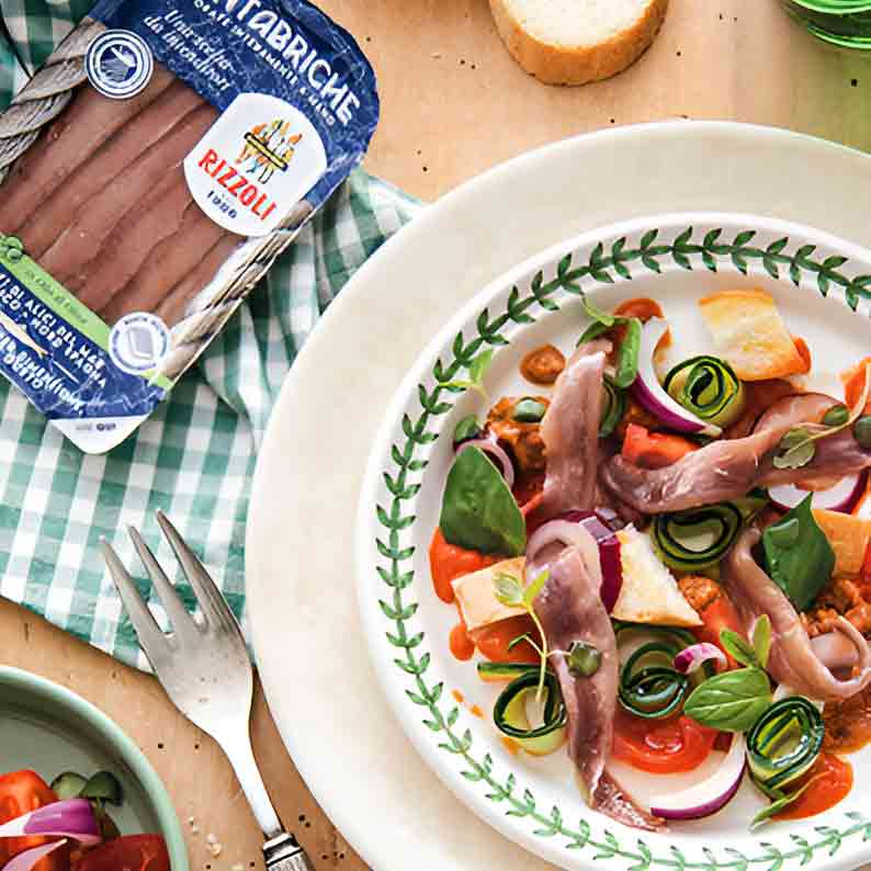 Teller mit Rizzoli Sardellen, Gemüse und Brot auf Tisch.