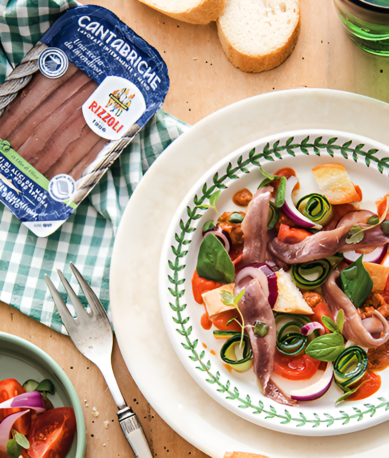 Teller mit Sardellen, Gemüse, Brot und Rizzoli-Verpackung.