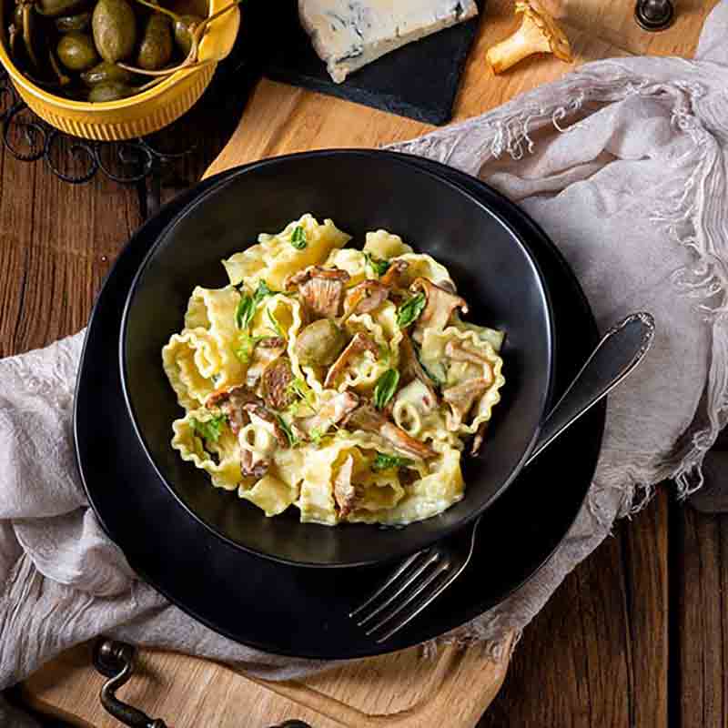 Pasta mit Pilzen, Oliven, Käse auf Holztisch arrangiert.