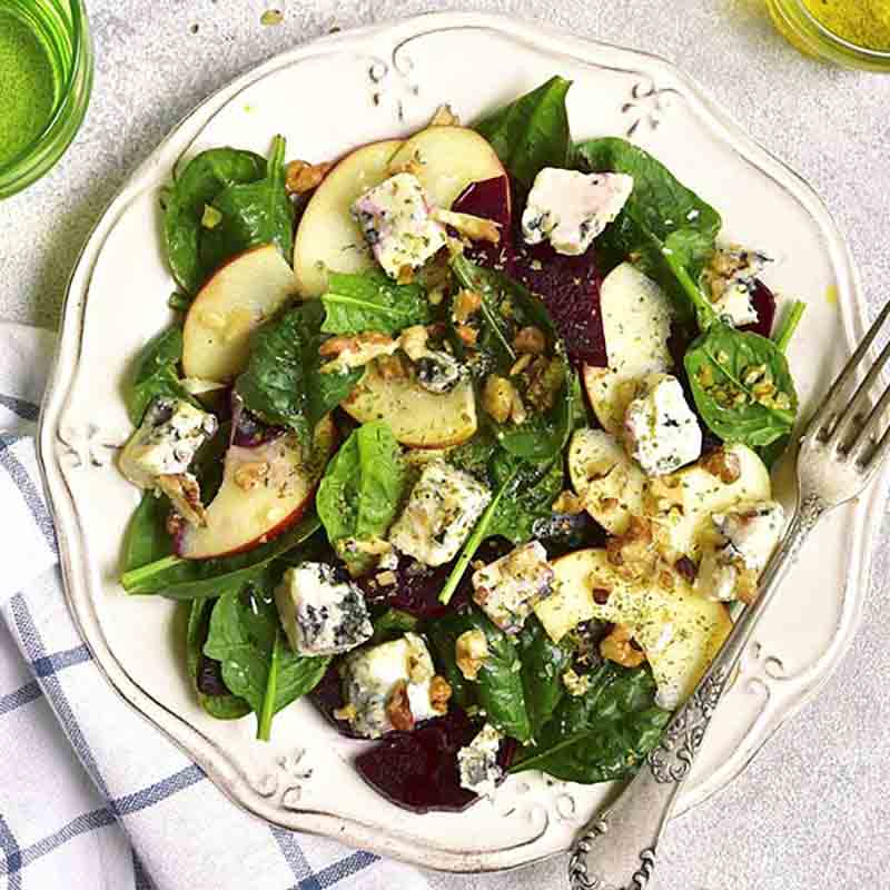 Salat mit Spinat, Käse, Nüssen und Apfelscheiben auf Teller.