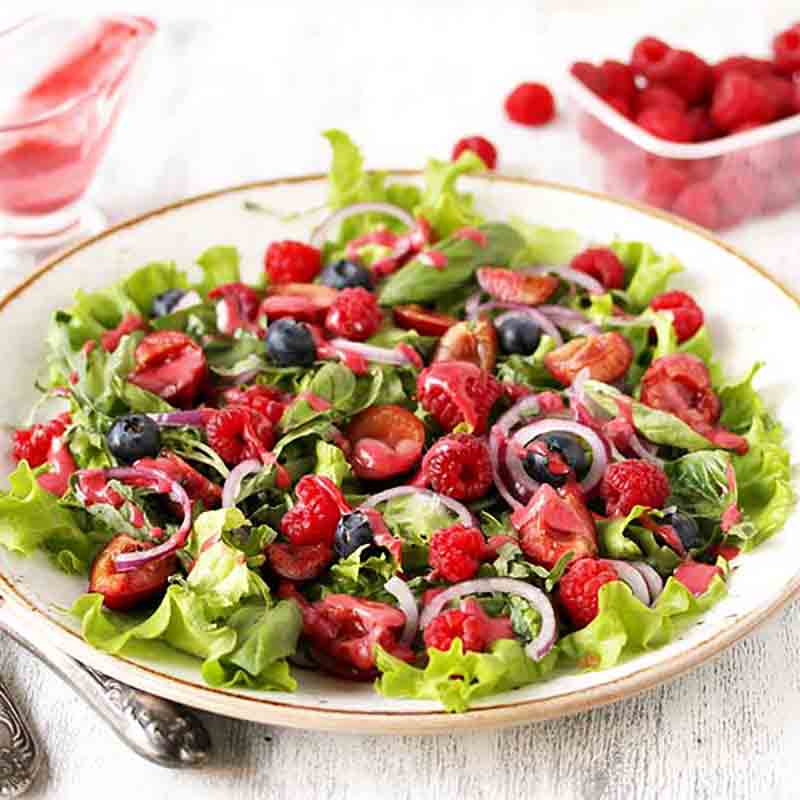 Salat mit Himbeeressig, Beeren und frischen Zutaten auf Teller.