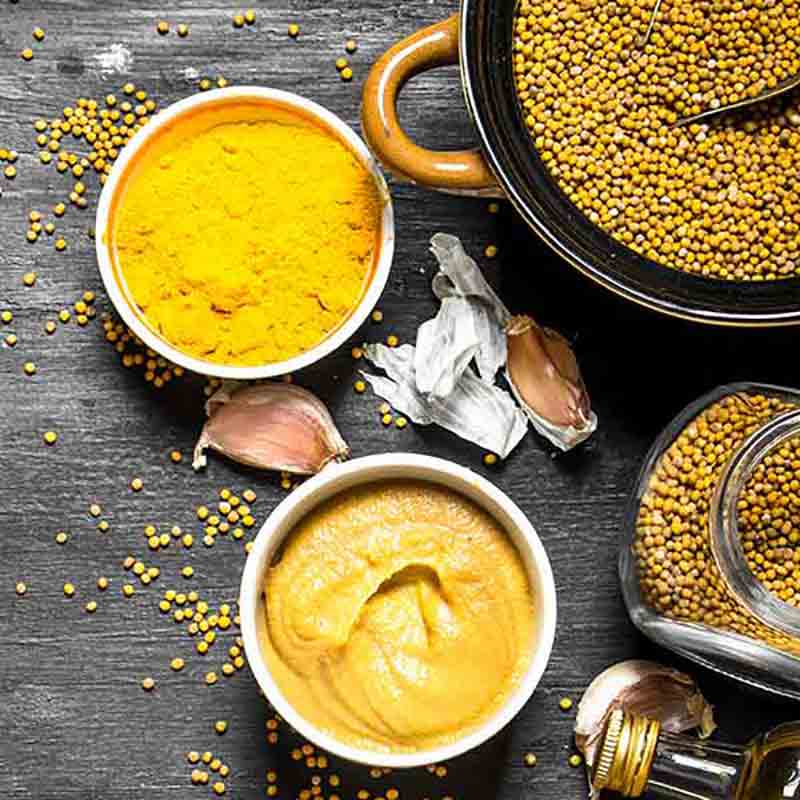 Senf, Senfkörner, Knoblauch auf dunkler Oberfläche arrangiert.