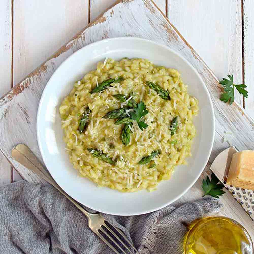 Risotto mit Spargel, Parmesan und Olivenöl auf Holztisch.