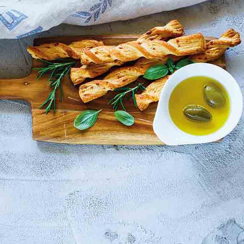 Holzbrett mit Gebäckstangen, Olivenöl und Kräutern.