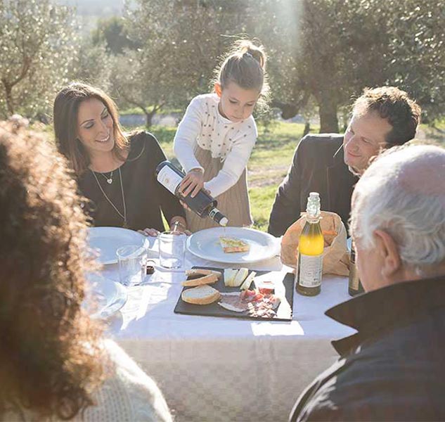 Familie genießt Mahlzeit im Freien mit Olivenöl und Wein.