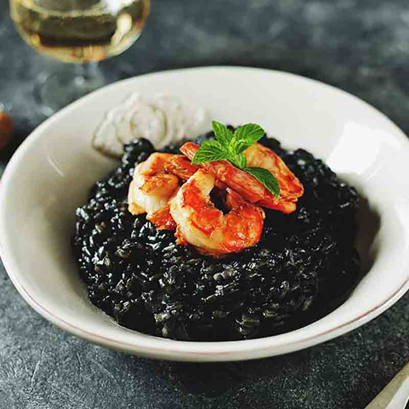Tintenfischrisotto mit Garnelen in weißem Teller, Glas Wein.