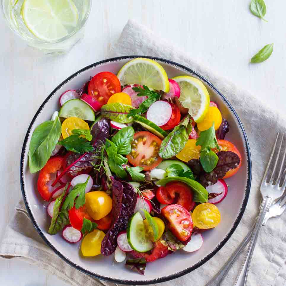 Salat mit Tomaten, Radieschen, Zitronenscheiben und frischen Kräutern.