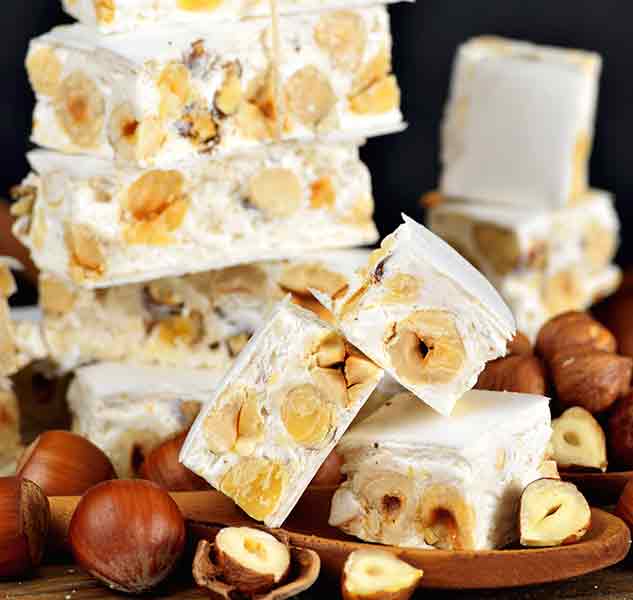Torrone-Nougat mit Haselnüssen auf Holzbrett arrangiert.