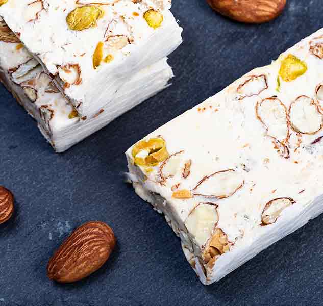 Nougat mit Mandeln und Pistazien auf Schieferplatte.